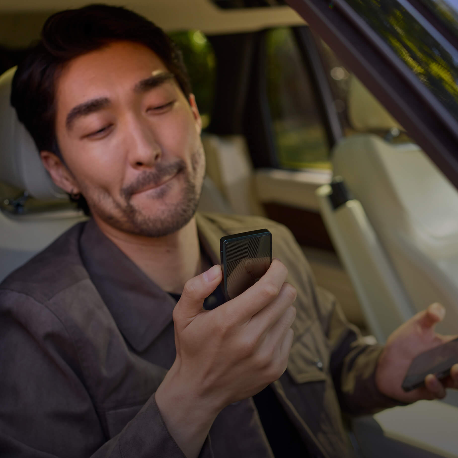 A man sitting and looking at a Trezor Safe 7 while holding a smartphone in his other hand.