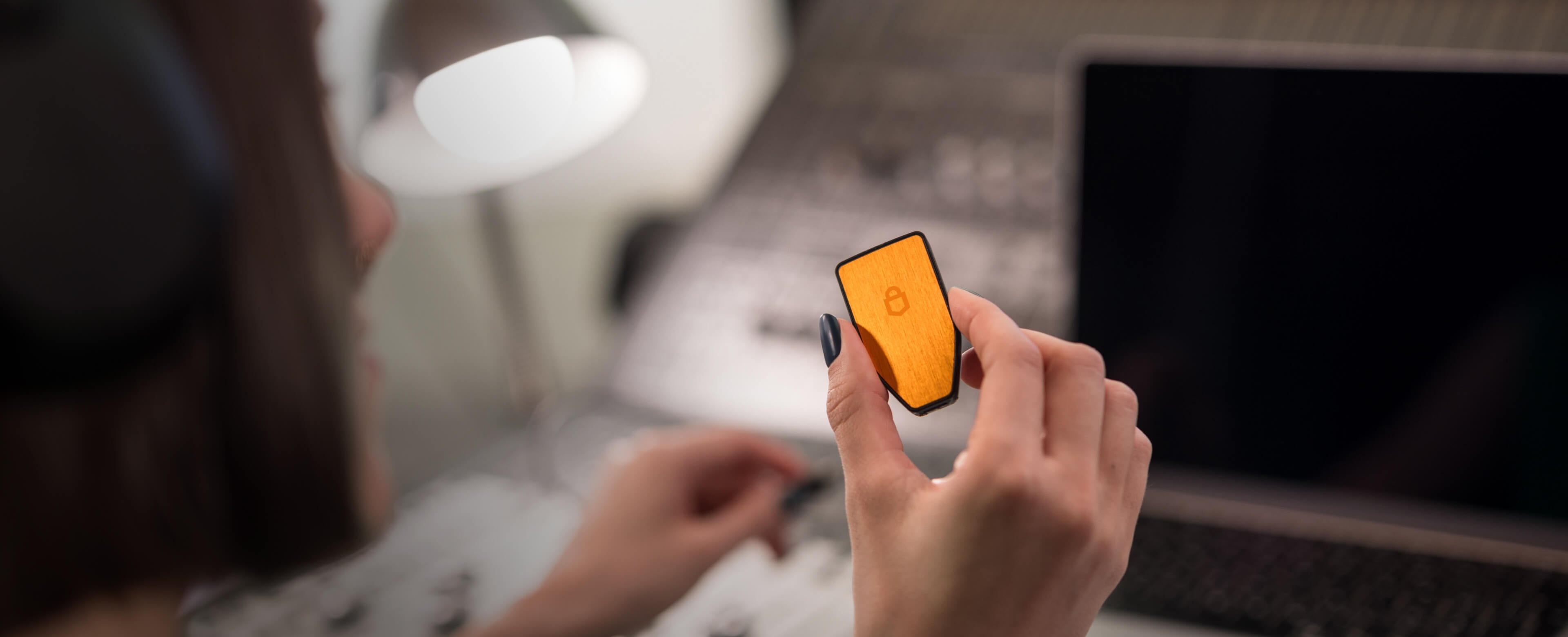 A person wearing headphones is holding a Trezor Safe 3 hardware wallet (BTC-only version) in front of a laptop and audio mixer.