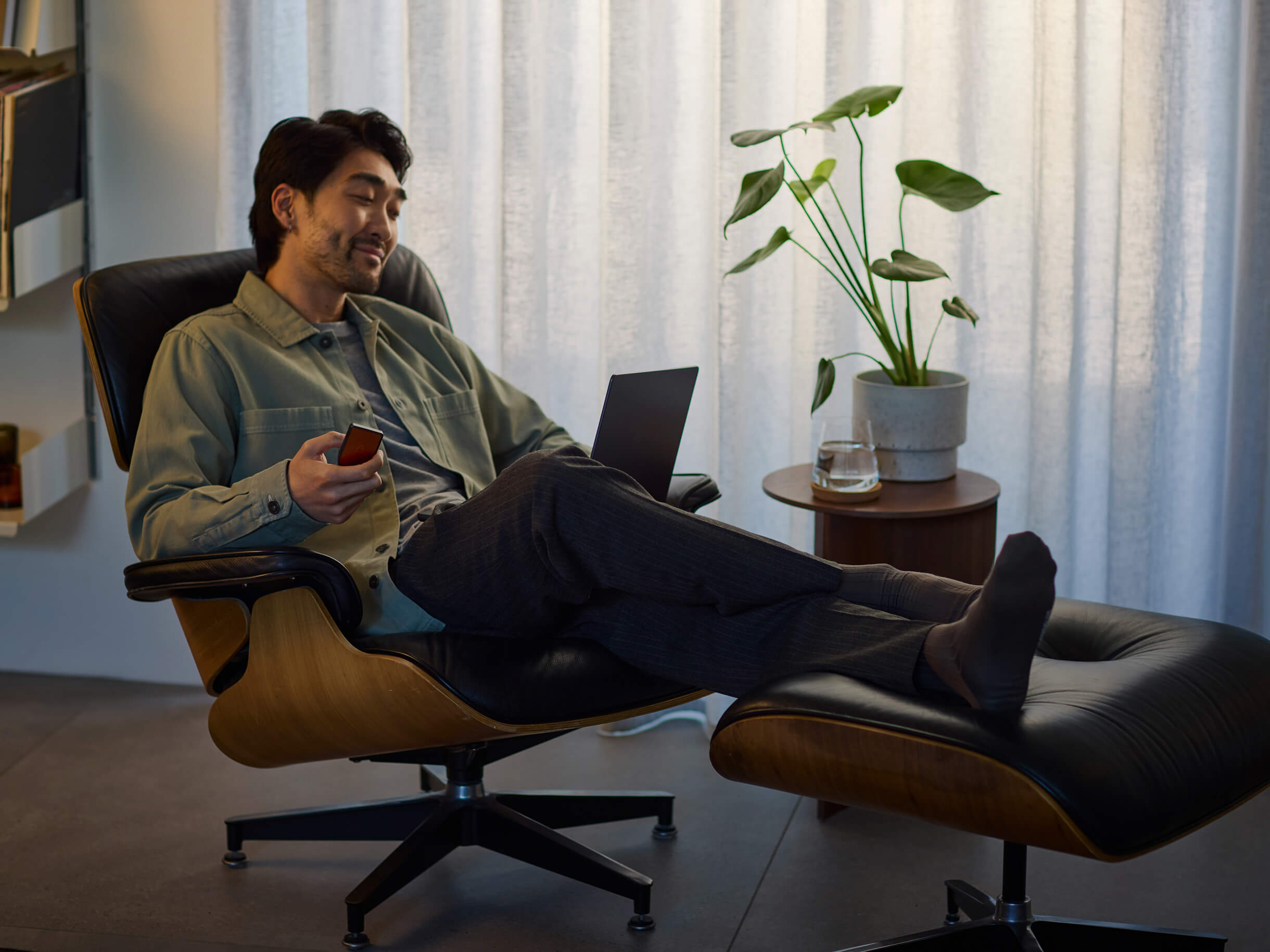 A man sits on a chair using a MacBook while holding a Trezor Safe 7 hardware wallet in one hand.